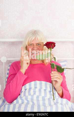 Happy woman in pink pajama sitting in bed with a red rose Stock Photo