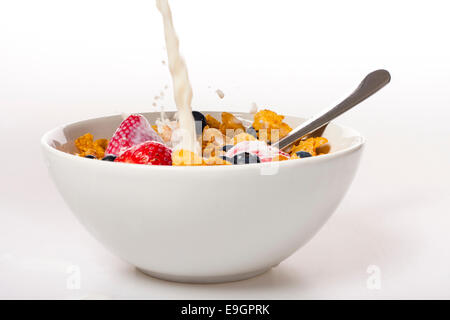 Milk poured over a fresh bowl of cornflakes with strawberries and blueberries. Stock Photo