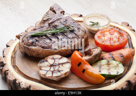 Portion of BBQ t-bone steak  served  on wooden board with  rosemary, mustard sauce  and grilled vegetables Stock Photo