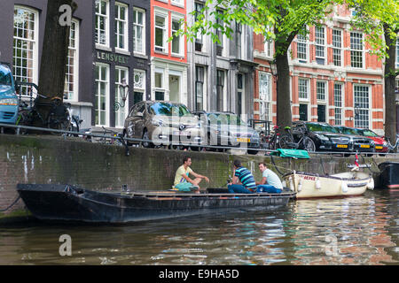 Three young men sitting on boat chatting on a canal in Amsterdam, Netherlands Stock Photo