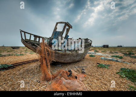 Old abandoned fishing boat and nets on shingle at Dungeness in Kent Stock Photo