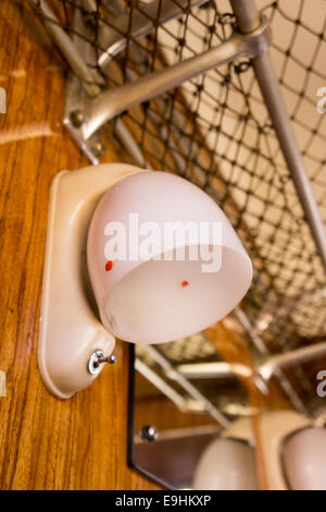 Vintage cabin light with frosted dome shade and wall switch, mounted beside luggage netting inside an old train or transport carriage Stock Photo