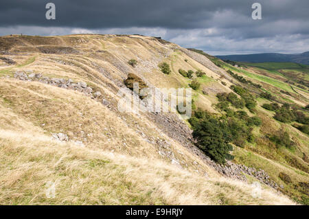 Cracken edge quarries near Chinley in Derbyshire. Sunshine on the foreground grasses. Dark sky overhead. Stock Photo