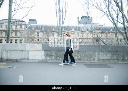 a young couple stroll along a street in paris dressed up warm in scarfs on a grey day Stock Photo