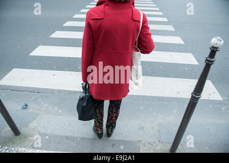 a woman in paris walks across a traffic crossing wearing a red jacket Stock Photo