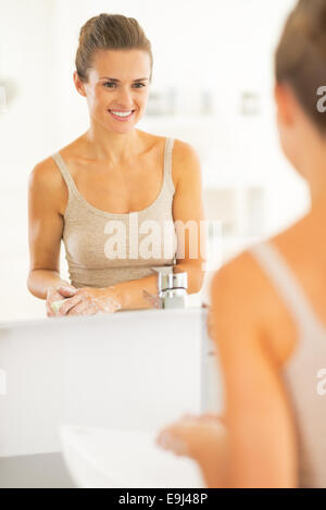 Happy young woman washing hands in bathroom Stock Photo