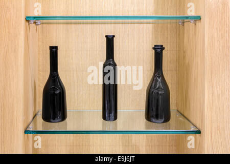 Three Empty black bottles on a glass shelves in a wooden cabinet Stock Photo