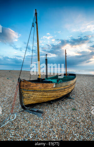 A small wooden sail boat on a shingle beach at sunrise Stock Photo