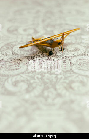 An antique yellow wooden toy airplane sits on a lace covered tabletop. Stock Photo