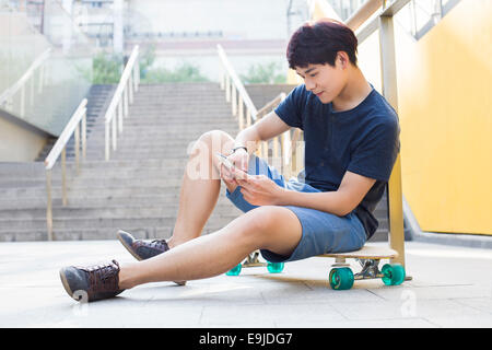 Young man sitting on skateboard using smart phone Stock Photo
