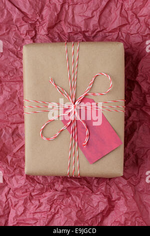 High angle closeup shot of a plain brown paper wrapped present tied with red and white string. The gift is on a piece of red tis Stock Photo