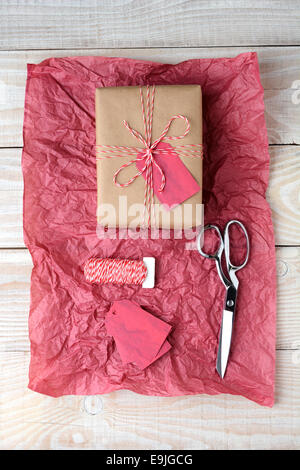 High angle shot of a plain brown paper wrapped present tied with red and white string. The gift is on a piece of red tissue. Stock Photo