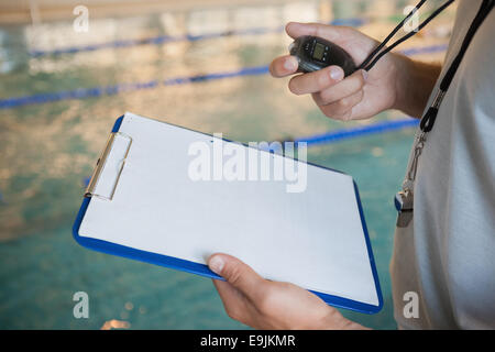 Swimming coach looking at his stopwatch by pool Stock Photo