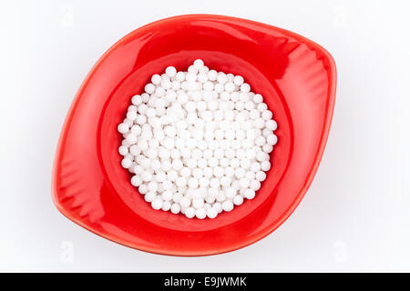 Overhead view of homeopathic medicinal pills in a red container on a white background. Stock Photo