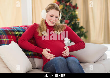 Beautiful pregnant woman holding her belly sitting on couch Stock Photo