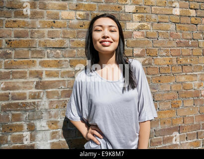 Portrait of confident young woman standing with hand on hip against brick wall