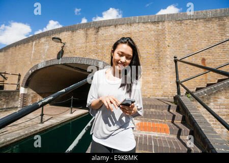 Smiling young woman using smart phone on stairs Stock Photo