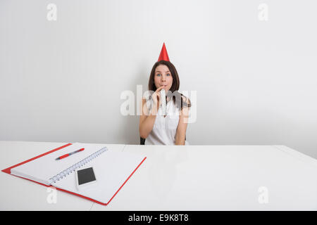 Portrait of happy businesswoman in party hat blowing horn at desk in office Stock Photo