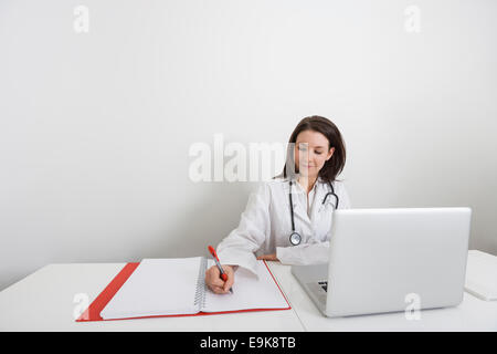 Female doctor writing on binder at desk in clinic Stock Photo