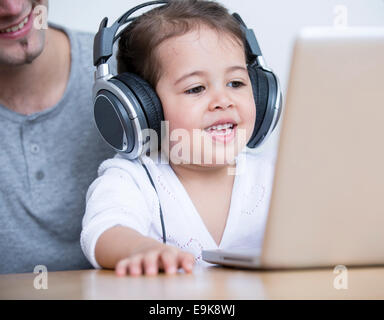 Little girl wearing headphones while looking at laptop with father at table in house Stock Photo