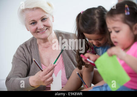 Portrait of senior woman helping granddaughters in making handicrafts at home Stock Photo