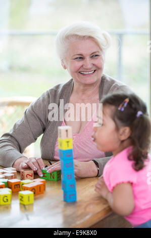 Happy grandmother looking away while granddaughter blowing stacked alphabet blocks in house Stock Photo