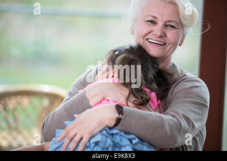Portrait of happy grandmother hugging granddaughter in house Stock Photo