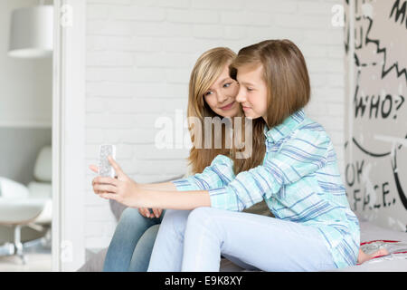 Cute sisters photographing themselves through cell phone at home Stock Photo