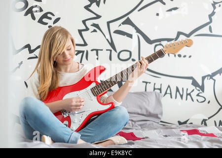 Full-length of teenage girl playing guitar in bedroom Stock Photo