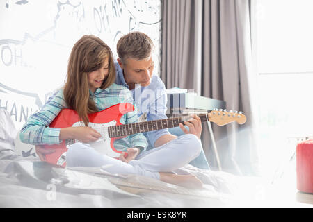 Father teaching daughter to play electric guitar at home Stock Photo