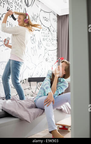 Girl watching sister singing into hairbrush in bedroom Stock Photo