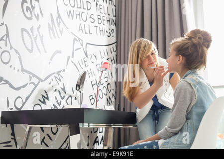 Teenage girl putting lipstick on sister at home Stock Photo