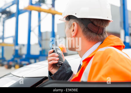 Middle-aged man using walkie-talkie while standing beside car in shipping yard Stock Photo