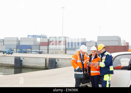 Workers using tablet PC beside car in shipping yard Stock Photo