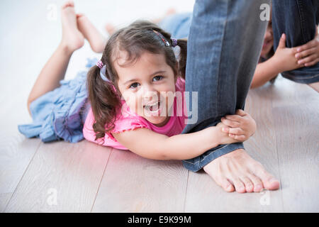 Portrait of playful girl with sister holding father's legs on hardwood floor Stock Photo