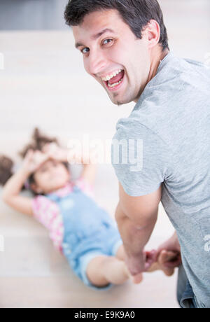 Rear view portrait of happy father dragging daughter on floor at home Stock Photo