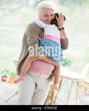 Portrait of loving grandmother carrying granddaughter at home Stock Photo