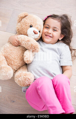 Happy girl with teddy bear lying on wooden floor at home Stock Photo