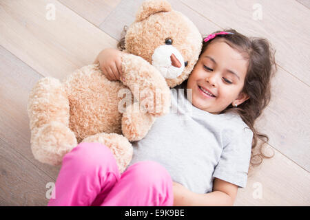 Girl with teddy bear lying on wooden floor at home Stock Photo