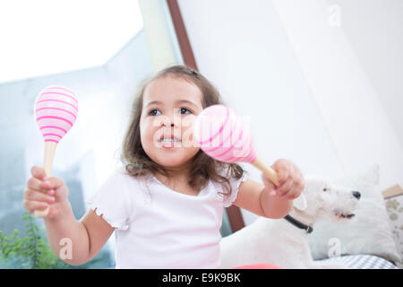 Cute girl playing with maracas while sitting beside dog at home Stock Photo
