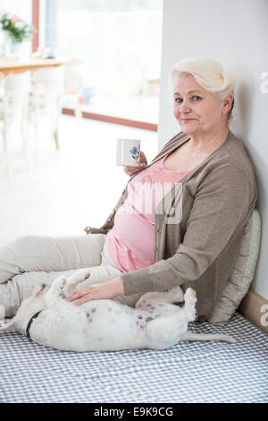 Portrait of happy senior woman having coffee while stroking dog at home Stock Photo