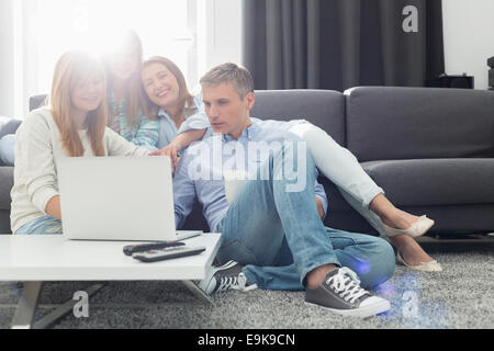 Happy parents with daughters using laptop in living room Stock Photo