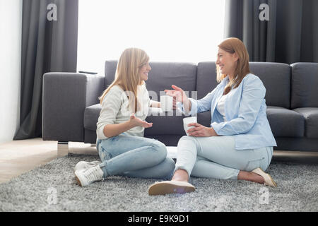 Happy mother and daughter talking while having coffee in living room Stock Photo
