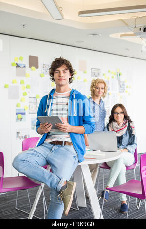 Portrait of creative businessman holding digital tablet with colleagues in background Stock Photo