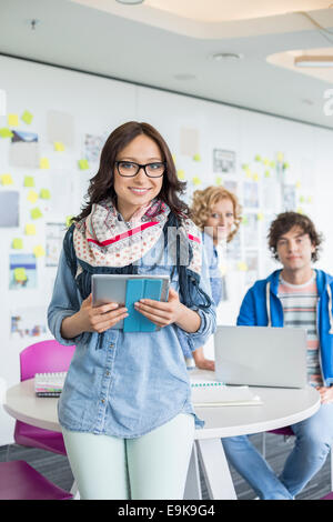Portrait of smiling businesswoman holding digital tablet with colleagues in background at creative office Stock Photo