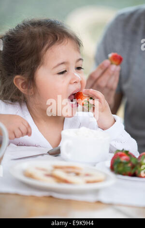 Cute little girl eating strawberry with father at breakfast table Stock Photo