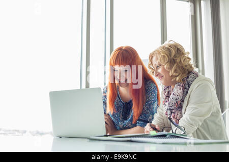 Happy creative businesswomen using laptop together in office Stock Photo