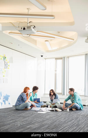 Businesspeople discussing while sitting on floor in creative office Stock Photo