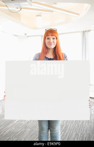 Portrait of confident businesswoman holding blank placard in creative office Stock Photo