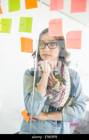Creative businesswoman reading sticky notes on glass wall in office